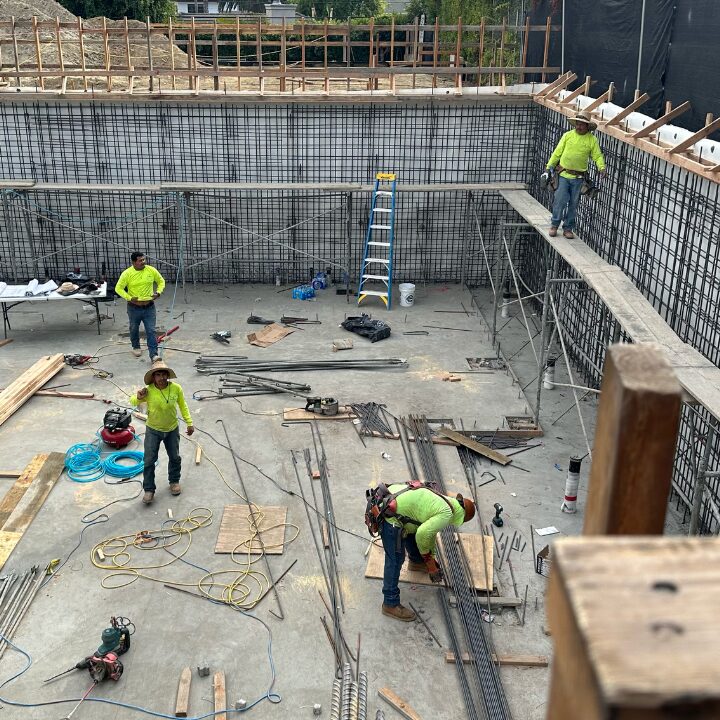 Workers assembling rebar framing inside a below-grade basement foundation site