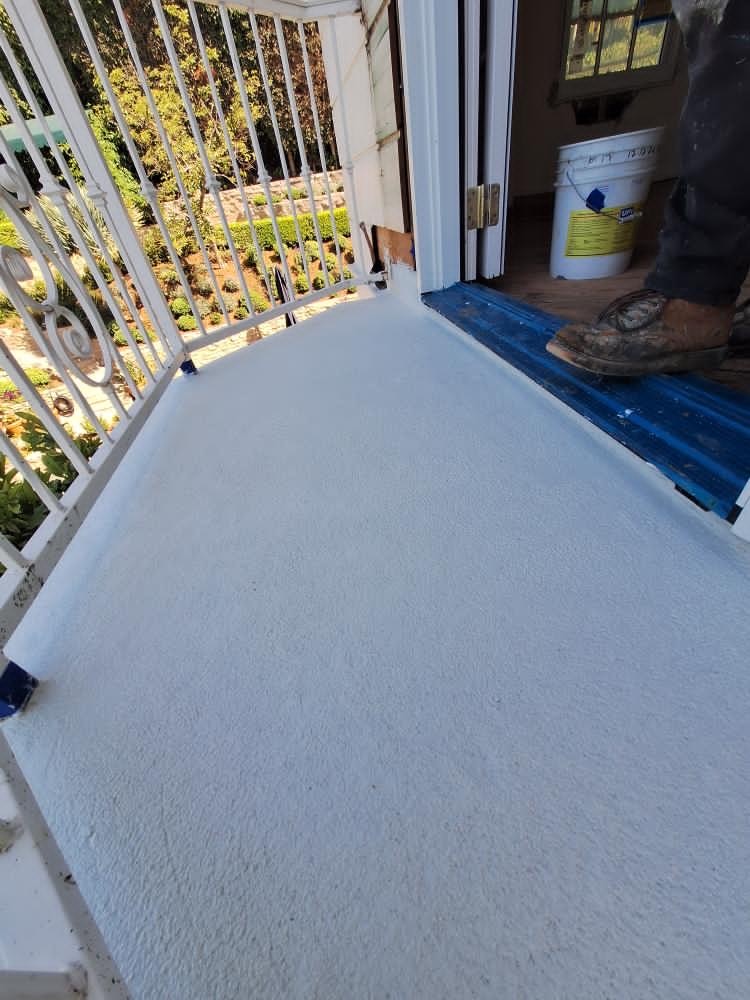 Clean white acrylic waterproofing coating applied near exterior doorway threshold on small balcony