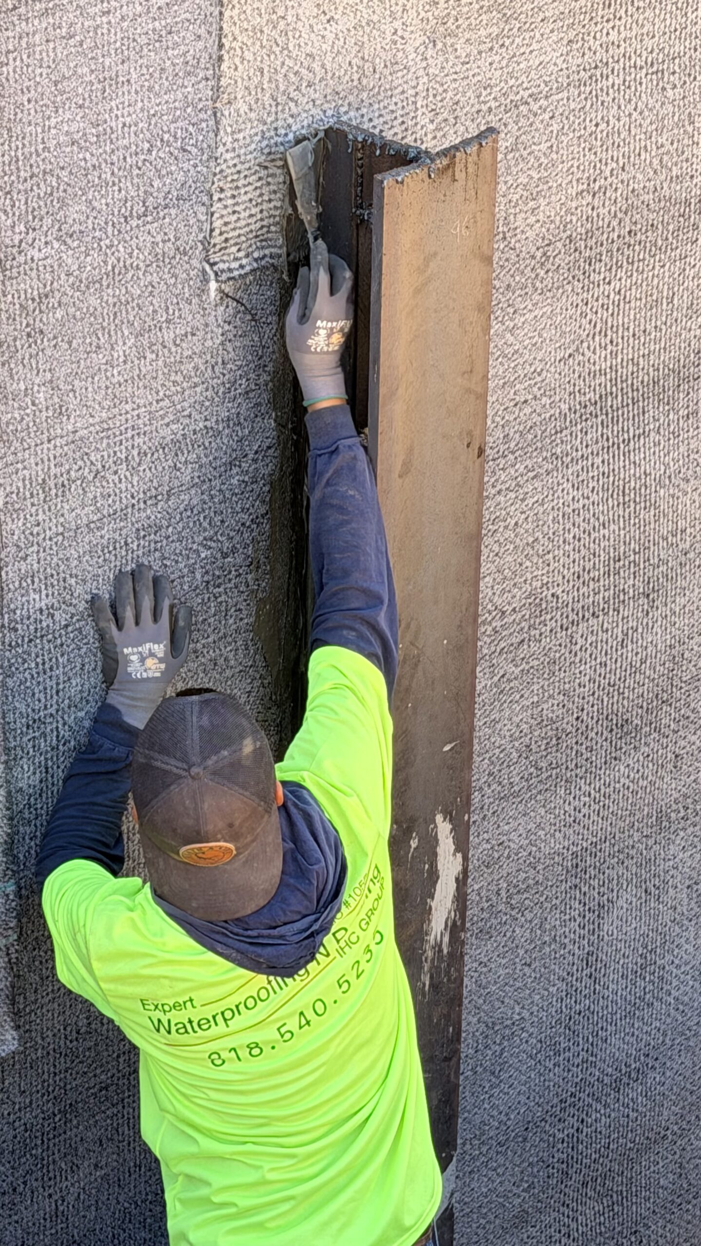 Worker installing corner detail sealant over textured waterproofing sheet membrane on foundation wall