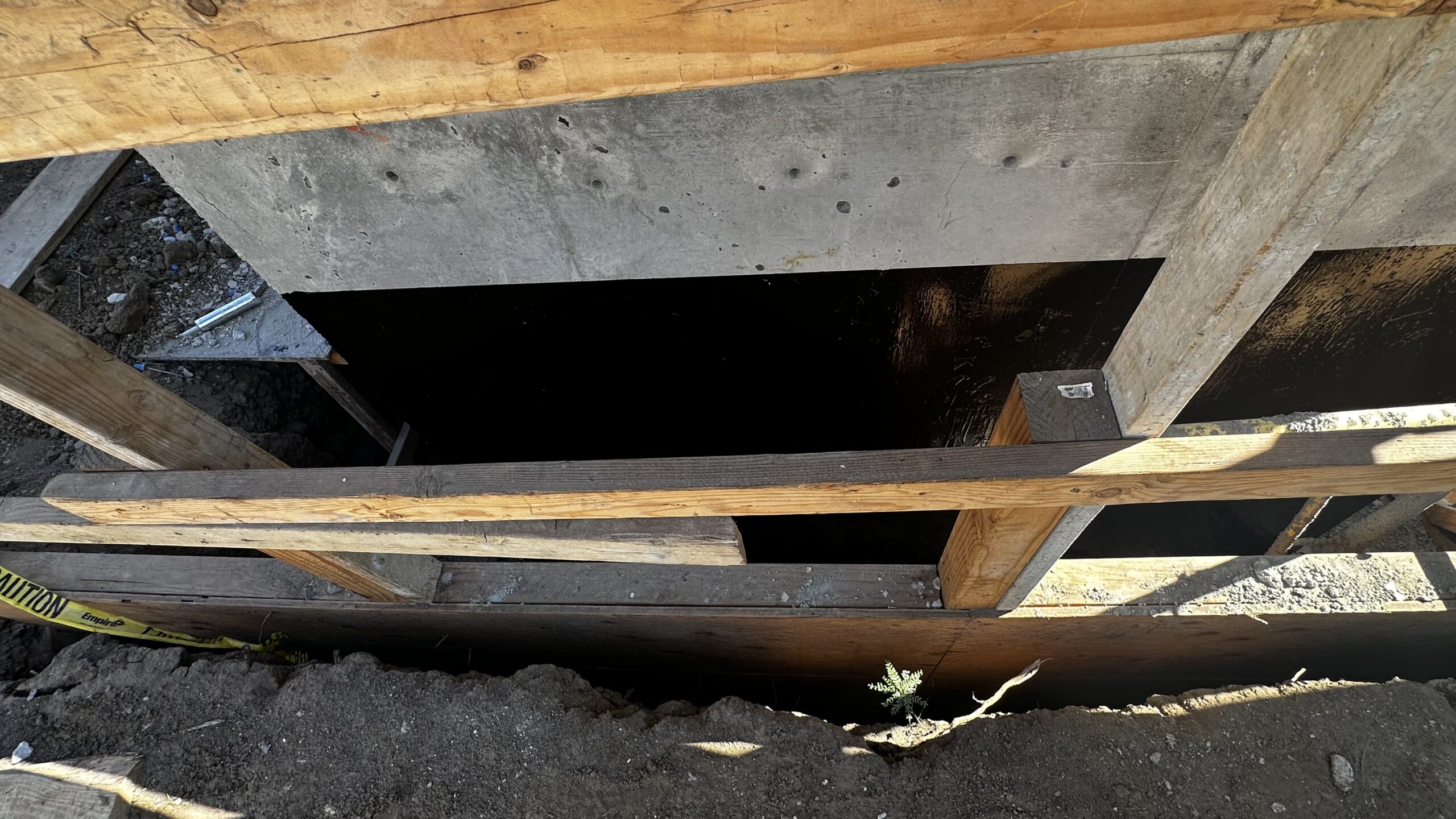 Looking down into dark elevator pit opening framed by wooden safety guardrails