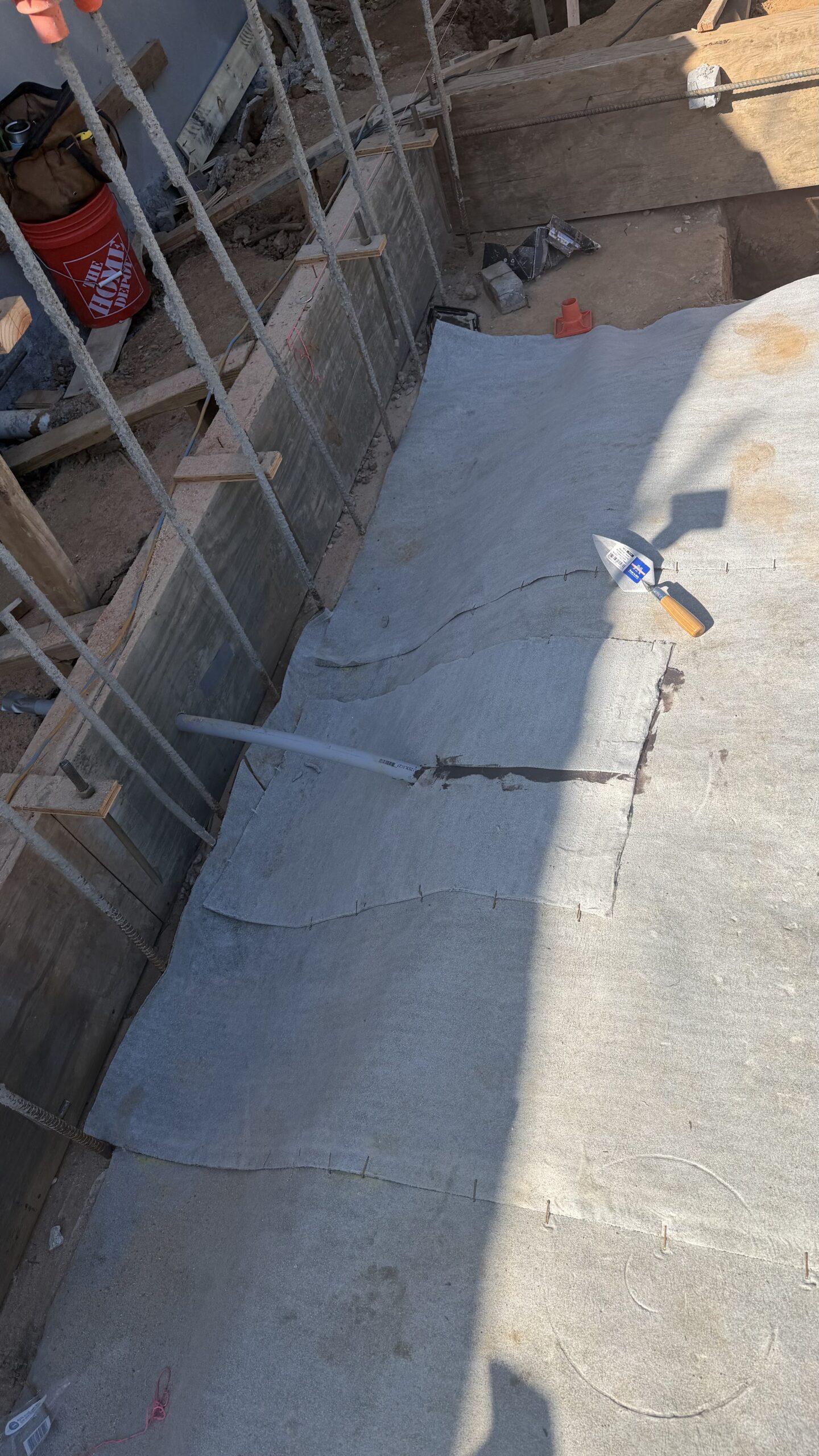 White sheet membrane installed along narrow concrete foundation trench with hand tools