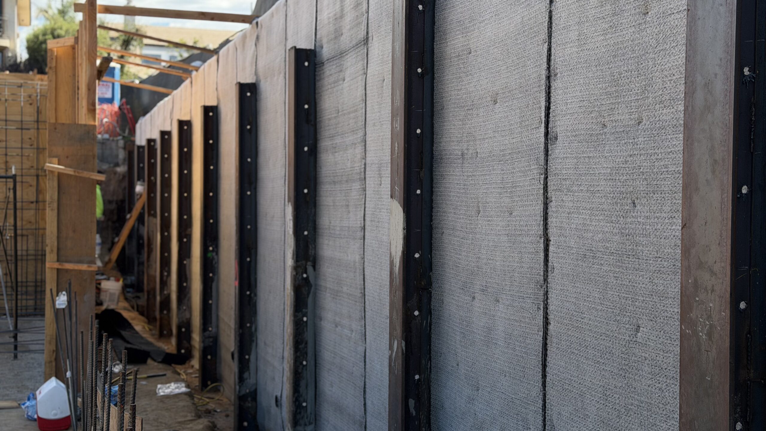 Concrete retaining wall with vertical steel beams and vertical joint sealing strips in an excavation trench