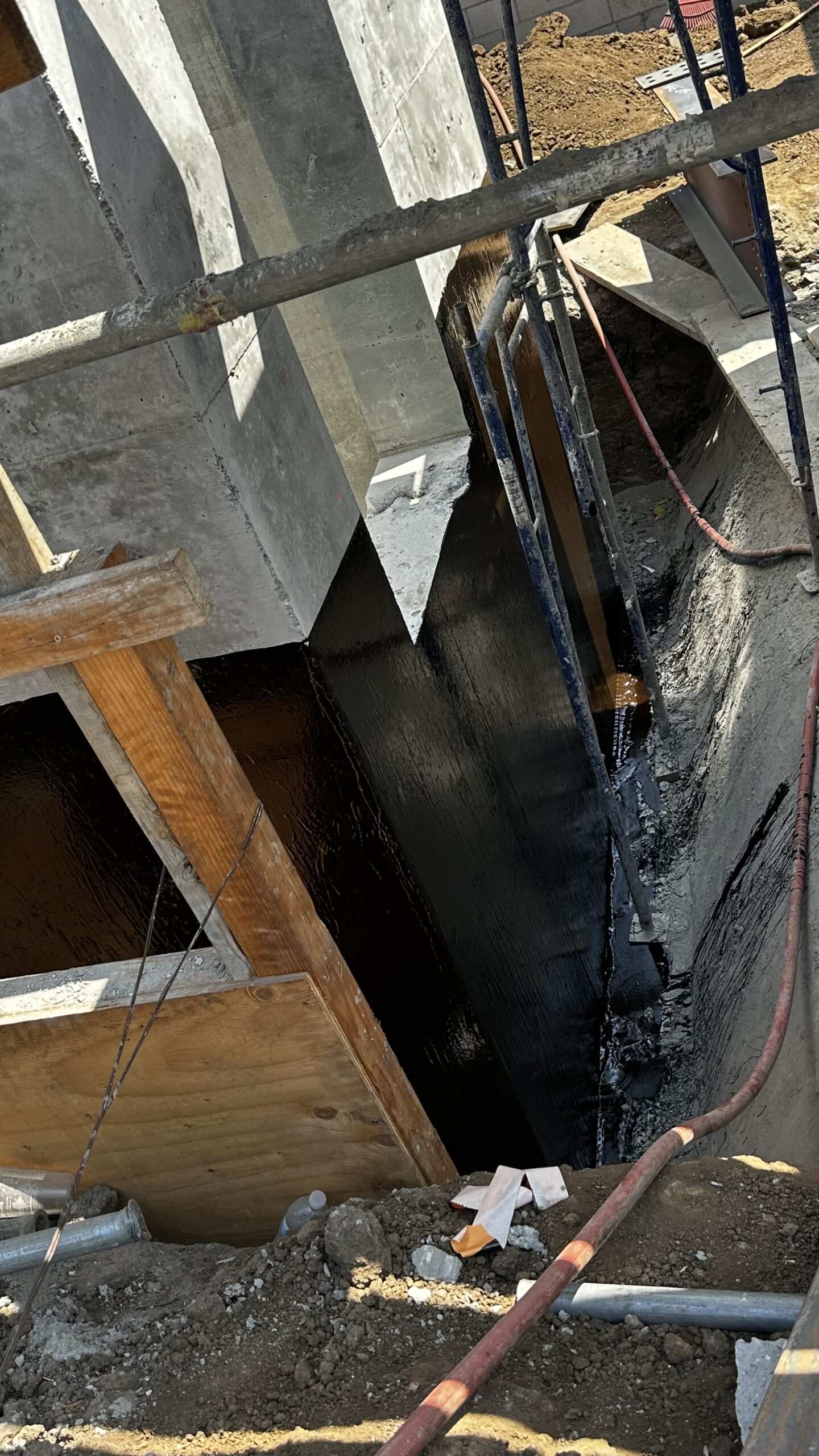 Close-up of black elastomeric waterproofing membrane on concrete elevator pit wall near foundation formwork