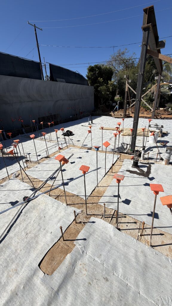 Concrete slab foundation under construction with orange capped rebar stakes at hillside site