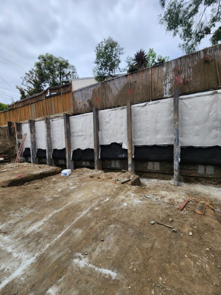 Long concrete foundation retaining wall under construction along excavated hillside site