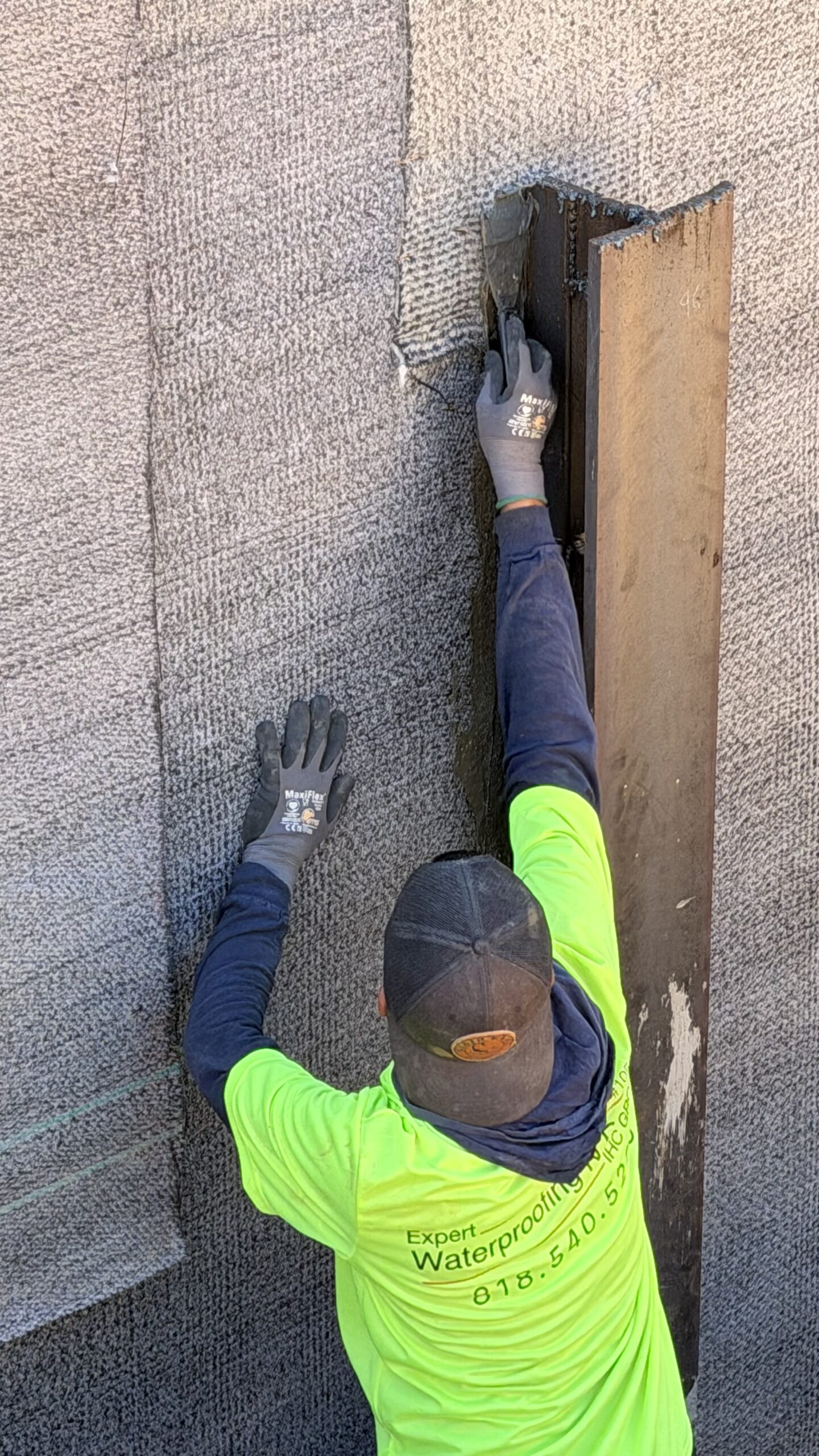 Worker installing textured protection drainage board on a vertical foundation retaining wall