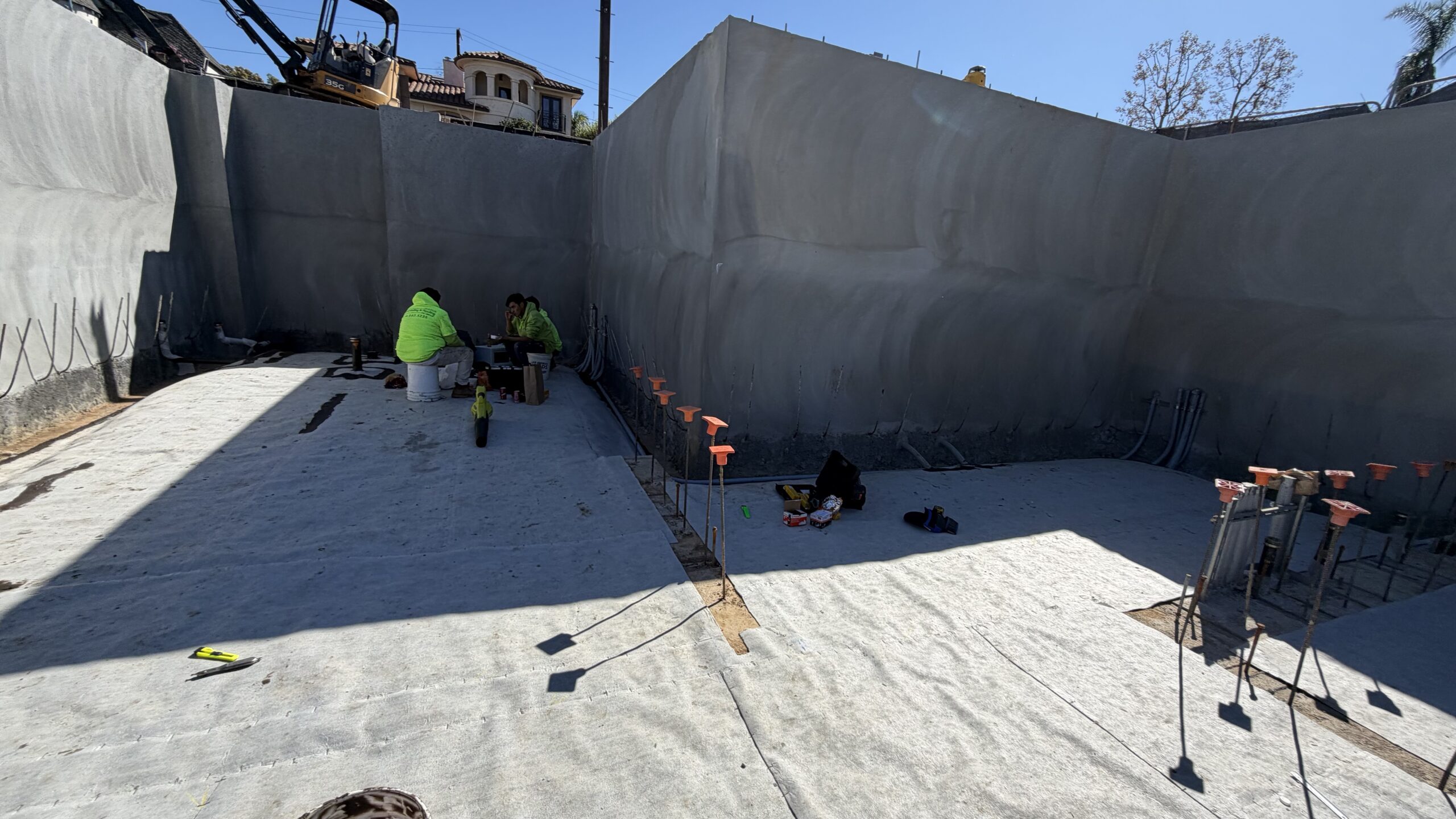 White under-slab waterproofing membrane installed across a deep basement floor excavation