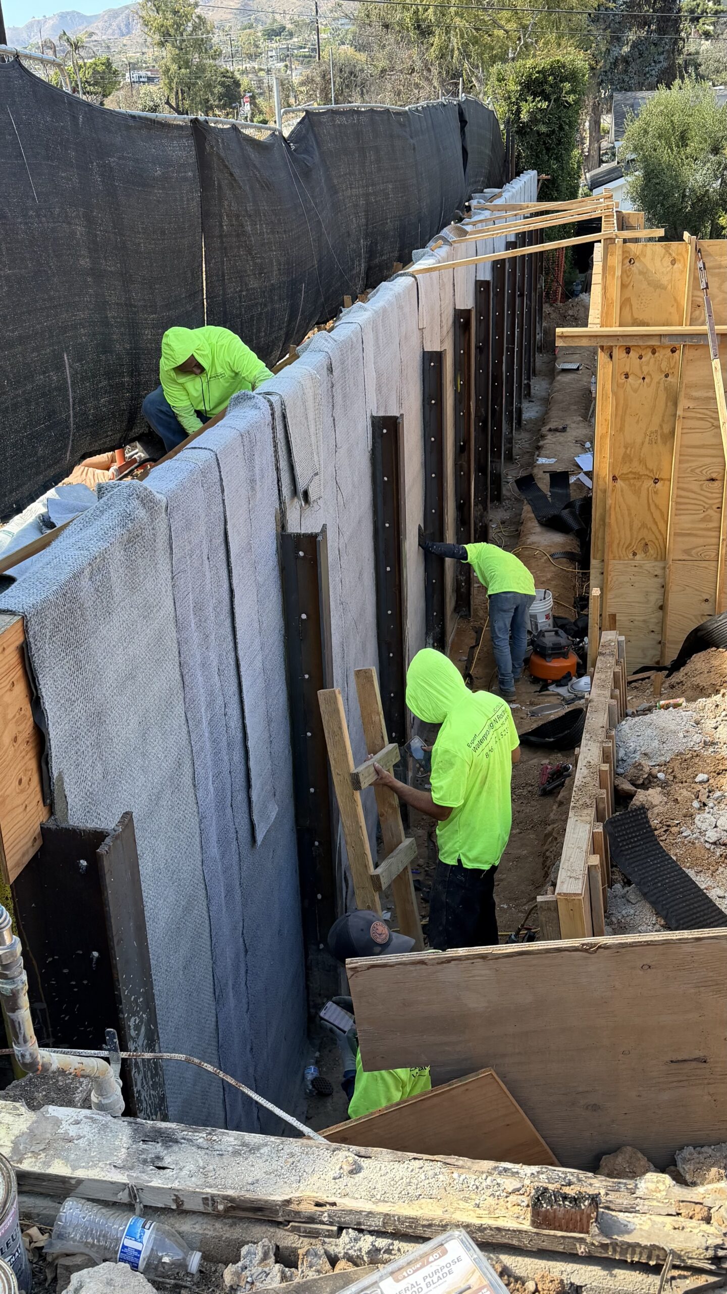 Workers in high-visibility neon green shirts working along shored foundation concrete wall panels