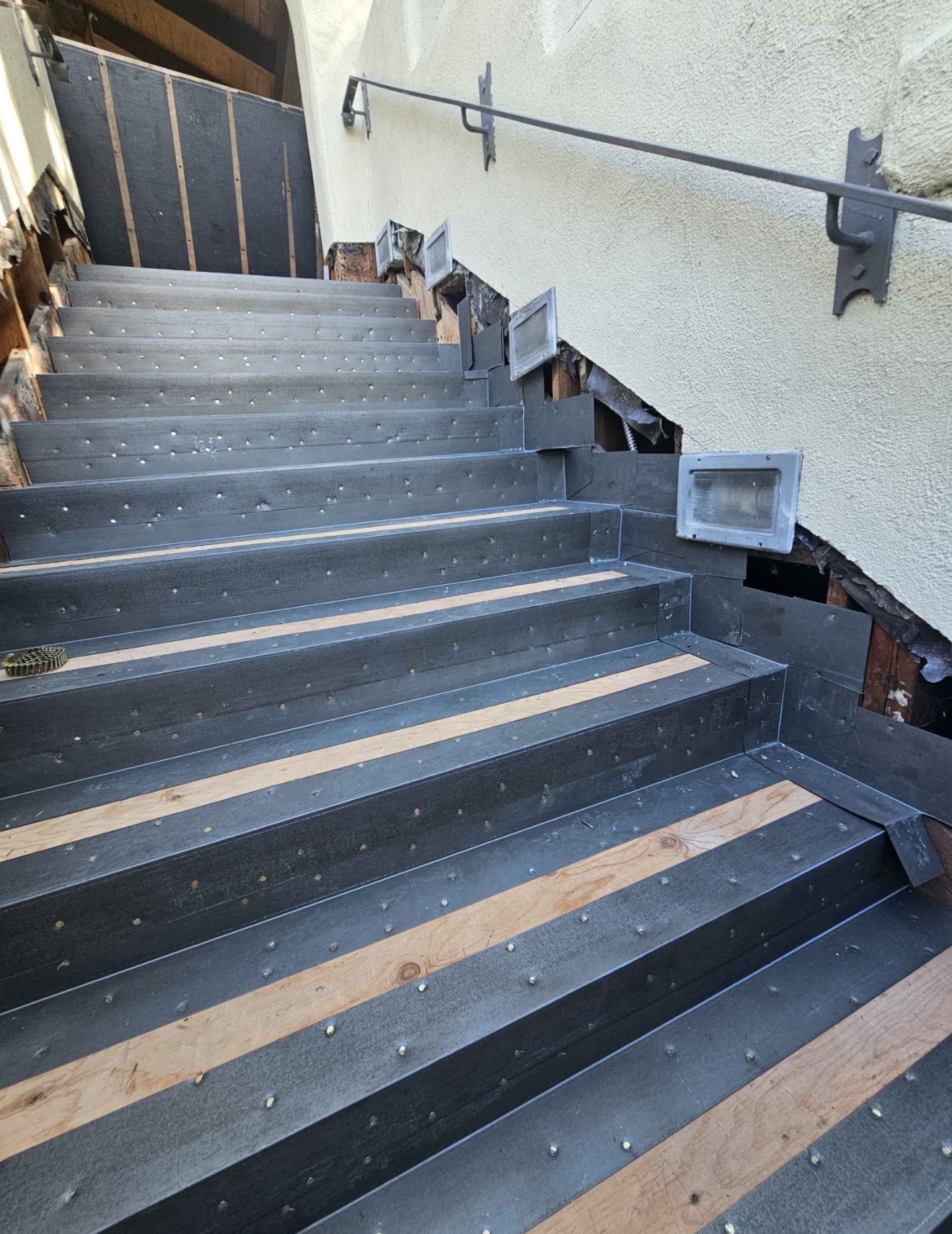 Angled view of exterior staircase treads lined with dark waterproofing membrane base prior to topcoat