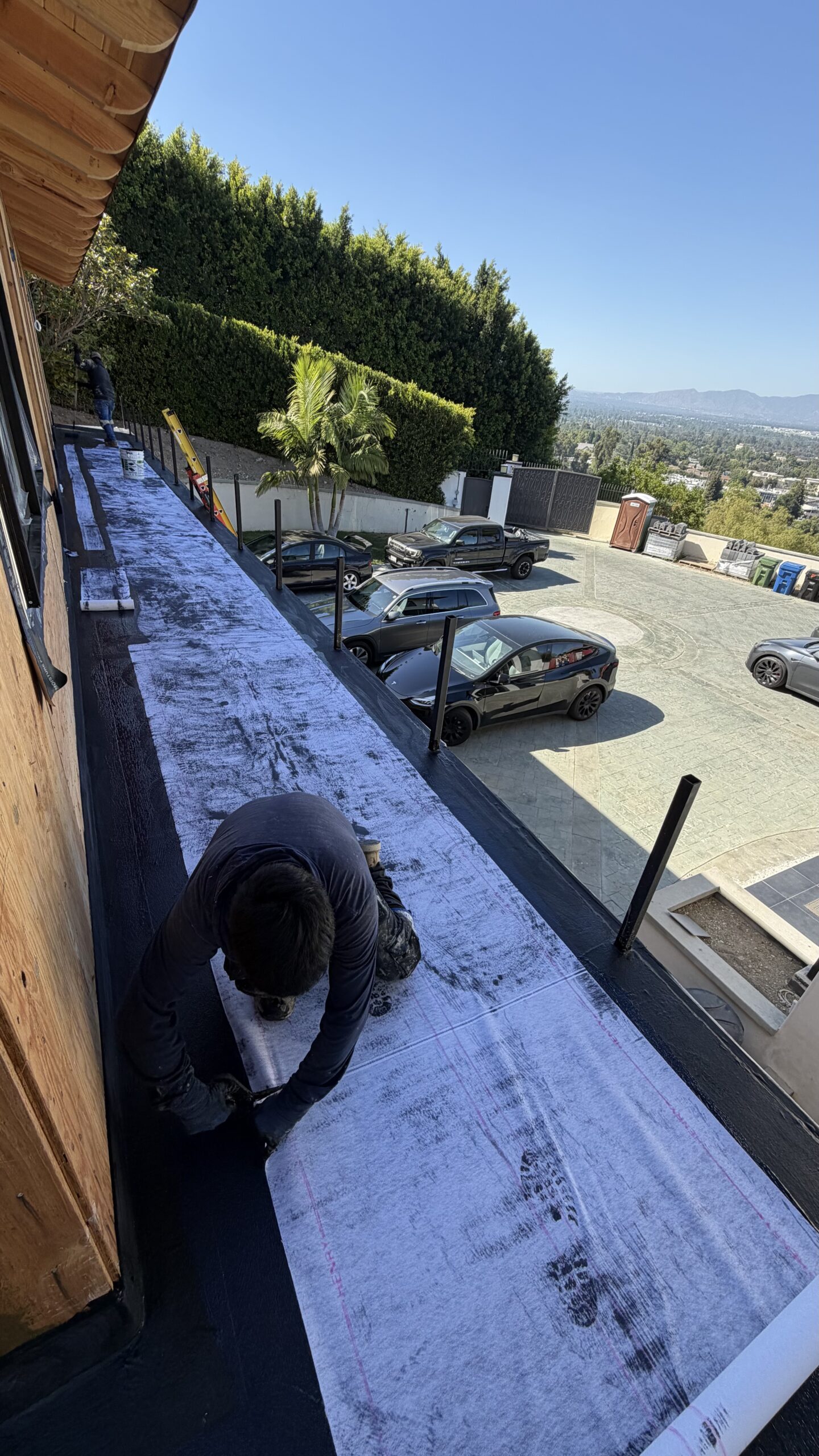 Contractor applying AVM 100 waterproofing system with polyester fabric over hillside upper deck