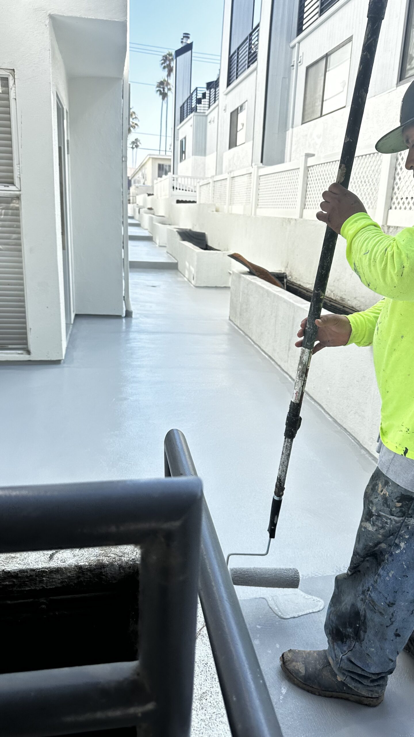 Worker using extension pole roller to apply liquid waterproofing coat on multi-unit walkway