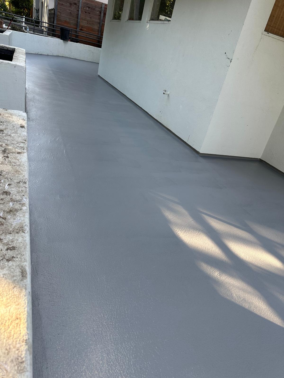 Smooth gray waterproofing base coat applied along outdoor residential access walkway