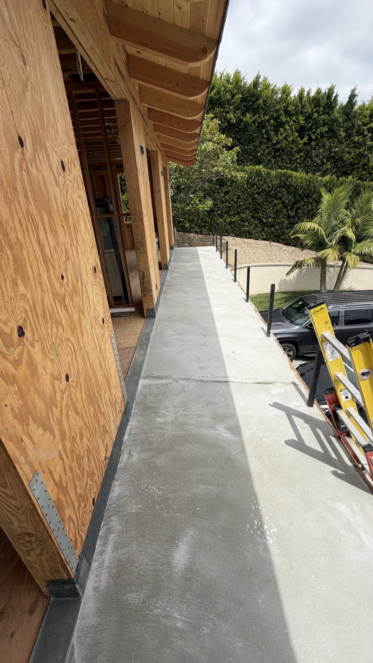 Concrete walkway substrate adjacent to unfinished plywood wall framing on residential building