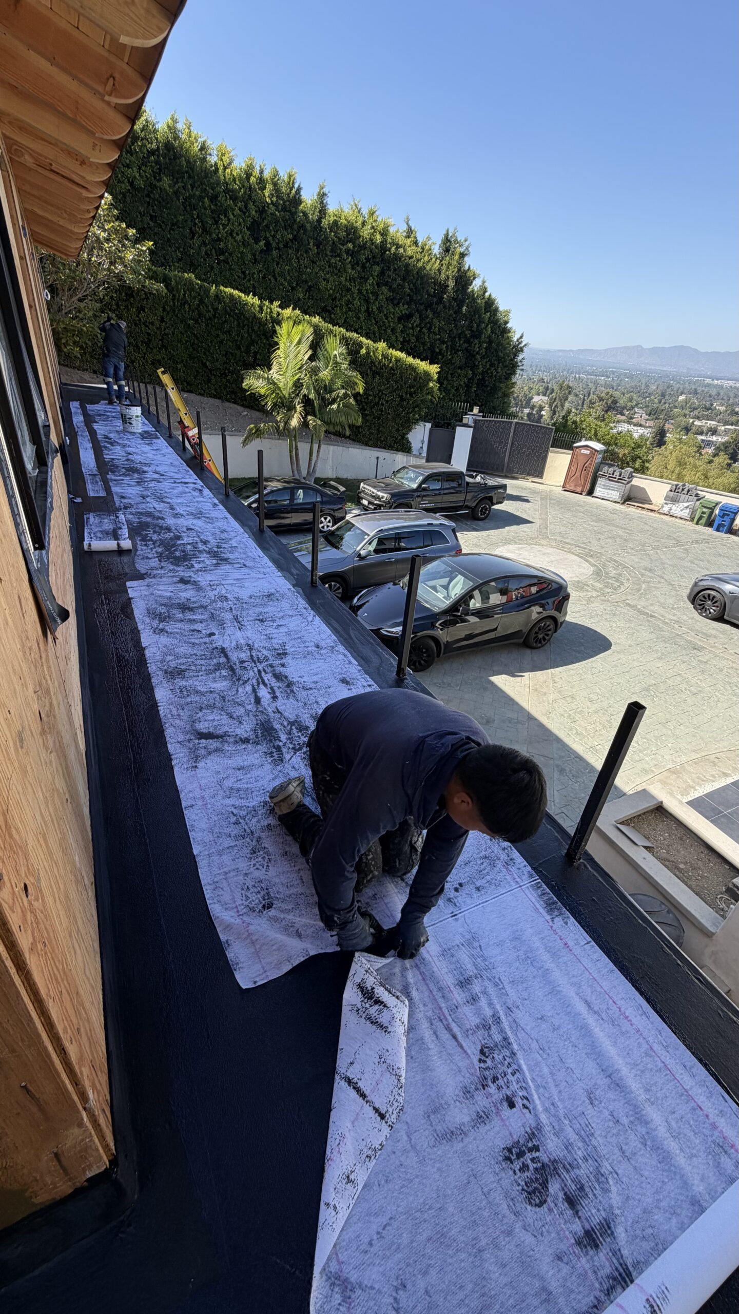 Waterproofing contractor pressing polyester fabric sheet onto long hillside upper deck surface